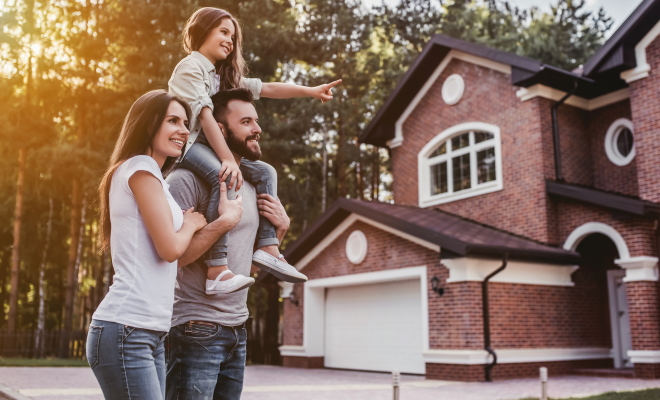 family of three standing infront of brick home